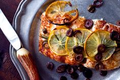 fish with olives and lemon slices on a metal platter next to a spoon