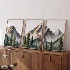 three framed mountain pictures on top of a wooden cabinet