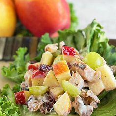 a salad with apples, grapes and chicken in it on a plate next to two oranges