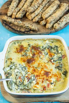 a casserole dish with spinach and cheese in it next to crackers