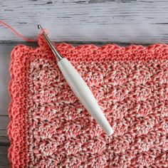 a crocheted square with a white crochet hook in the middle and yarn on top