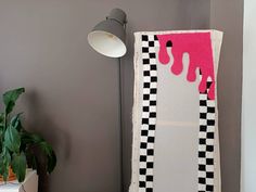 a pink and black piece of art on a wall next to a potted plant