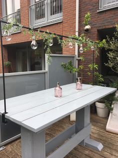 an outdoor table with two pink vases on it and lights hanging from the ceiling