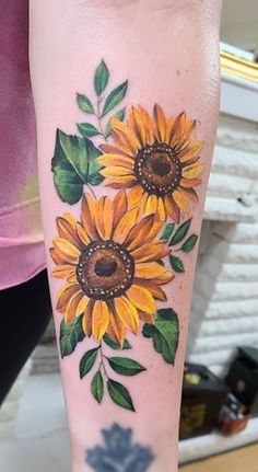 a sunflower tattoo on the arm with leaves and flowers painted on it's side