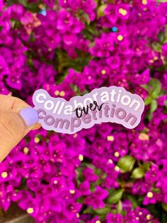 someone holding up a sticker with the word collaboration written on it in front of purple flowers