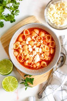 a bowl of tortellini soup on a cutting board with limes and cilantro