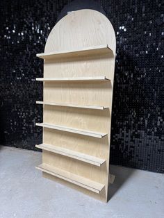 a wooden book shelf sitting in front of a black mosaic wall with silver sequins