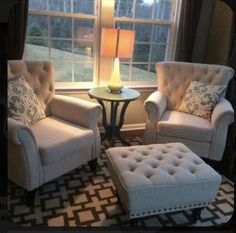 two chairs and a foot stool in front of a window with a lamp on it