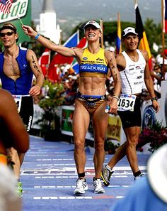 two women in bikinis are running on a race track with other people watching from the sidelines