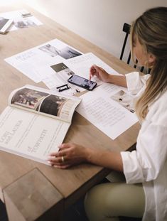 a woman sitting at a wooden table with papers and cell phone on top of it