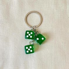 three green dice keychains with white dots on them are hanging from a metal ring