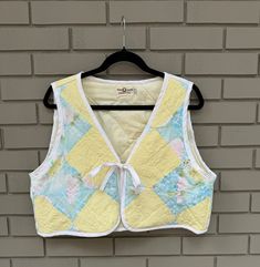 This vest was handmade from vintage quilt in yellows, florals and pastels. The vest has a front tie made from cotton bias tape which also is the border of the vest. Would make an excellent layer over sweaters and blouses in the colder months.  Size M - slightly oversized fitting. Please measure one of your existing garments to compare.  Measurements (taken while laying flat): pit to pit: 21 inches  base of neck to base of vest: 18  inches  apex of shoulder to pit: 12 inches  (arm hole) ------------------------------------------------------------------------- Please note: hand washing recommended to extend the life of the piece. Due to the nature of the pre-loved quilt, imperfections are expected (small stains or marks). Photos may not accurately reflect the true vibrancy of the colours and Quilt Vest, Clothing Upcycle, Vintage Quilt, Bias Tape, Quilted Vest, Patchwork Quilt, Vest Outfits, Vintage Quilts, Patchwork Quilts