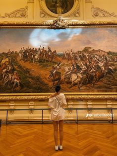 a woman standing in front of a large painting with horses on it's wall