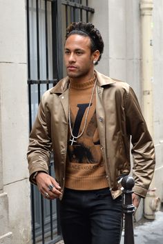 a man with dreadlocks walking down the street wearing a tan jacket and brown sweater