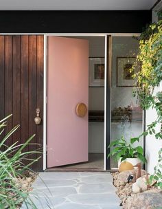 a pink door in front of a house with plants and rocks on the side walk