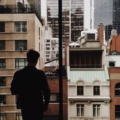 a man standing in front of a window looking out at the cityscape and skyscrapers