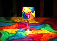 a wine glass sitting on top of a table covered in multicolored liquids