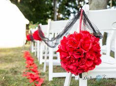 red flowers are hanging from the back of white chairs at an outdoor wedding ceremony with black ribbon