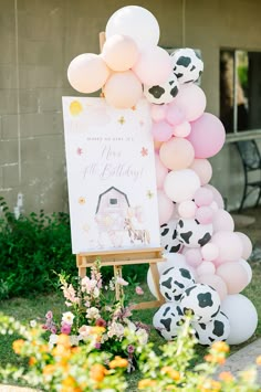 a sign with balloons attached to it in front of some flowers and plants on the grass