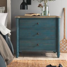 a blue chest of drawers in a bedroom with flowers on the top and an open book on the bottom