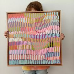 a person holding up a painting with different colored lines on the paper in front of their face