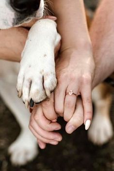 two people holding hands with a dog on the other hand and a ring in their left hand