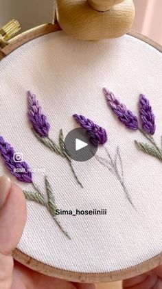 someone is stitching lavender flowers on a wooden hoop