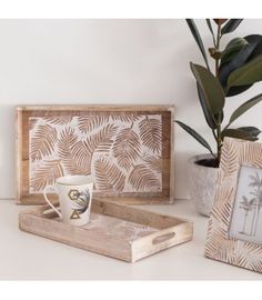 a wooden tray with two mugs and a palm tree print on it, sitting next to a potted plant