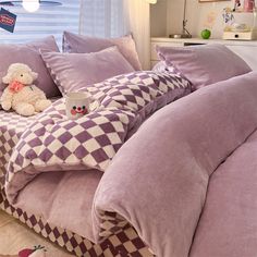 a teddy bear sitting on top of a bed with purple comforter and pillow cases