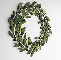 a wreath made out of green leaves and olives hanging on a wall with white background