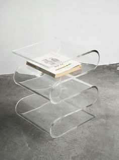 a clear table with a book on it and a white wall in the back ground