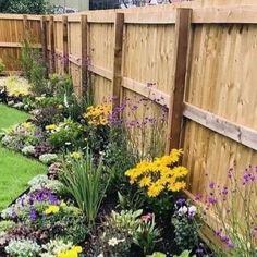 a garden filled with lots of colorful flowers next to a wooden fence and green grass