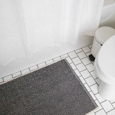 a white toilet sitting next to a black and white bath rug on top of a bathroom floor