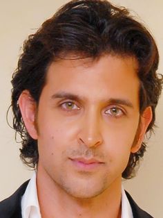 a close up of a person wearing a suit and tie with curly hair, looking at the camera