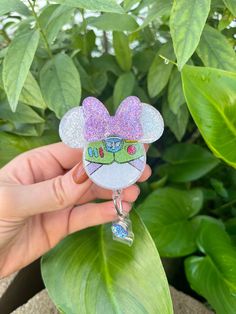 a hand holding a glass charm with a cartoon character on it's face in front of some plants