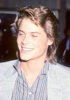 a close up of a person wearing a suit and smiling at the camera with other people in the background