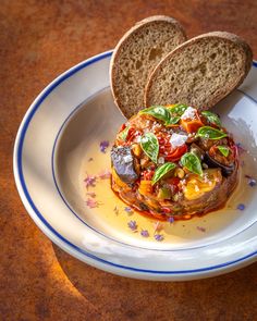 an eggplant and tomato dish on a white plate with two slices of bread