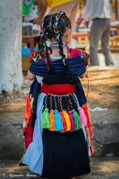 a woman with braids is walking down the street wearing a colorful dress and headdress