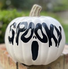 a painted pumpkin sitting on top of a brick wall with the word ghost written on it