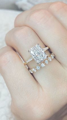 a woman's hand holding an engagement ring with two diamonds on it and a diamond band