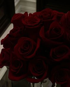 a vase filled with red roses sitting on top of a table next to a mirror