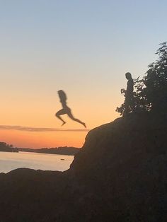 a person jumping into the air from a rocky cliff near water at sunset or dawn