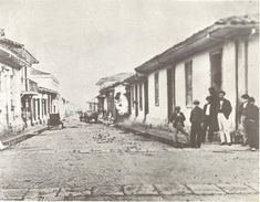 an old black and white photo of people standing on the street in front of buildings