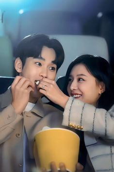 a man and woman sitting next to each other while eating food from a yellow cup