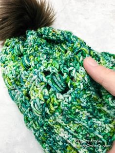 a hand is holding onto a green and white knitted hat