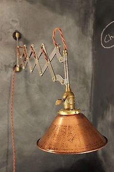 a copper colored lamp hanging from the side of a blackboard with writing on it