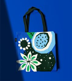 a blue bag with white and green flowers painted on the front is against a bright blue background