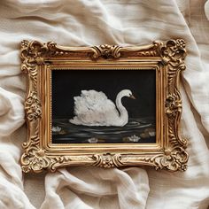 a painting of a white swan floating on top of water in a gold framed frame