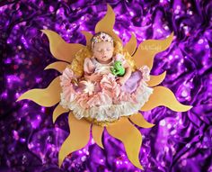 a baby doll sitting on top of a purple and yellow sunflower with glitters in the background