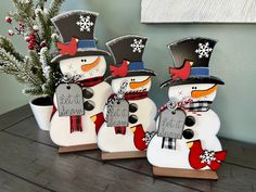 three snowmen with hats and scarfs are standing next to a small christmas tree